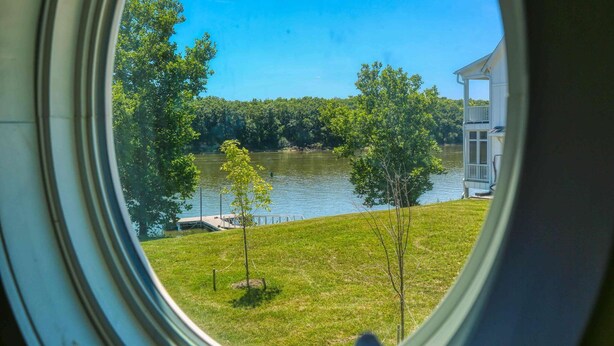 Vista de un lago a través de una ventana, con un muelle y un edificio pequeño en la orilla.