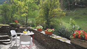Un espace extérieur aménagé avec des murs en pierre, des plantes en pot et une table entourée de chaises.