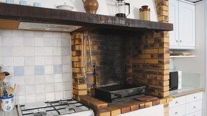 Une cuisine avec un four en briques, des armoires blanches et une cuisinière à gaz.