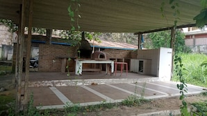 An outdoor patio with a brick oven, a table, and a red stool. - Hotel Jota (São Sebastião)