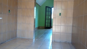 A corridor with tiled walls and floor, leading to a door with a glass panel. - Hotel Jota (São Sebastião)