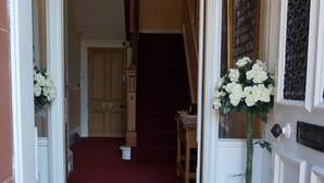 A hallway with a patterned floor, a red carpet, a wooden door, and a potted plant. - Lindean Guest House (Dumfries)
