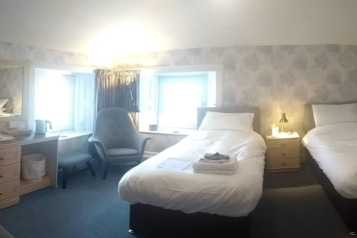 A hotel room with a desk, two single beds, a wardrobe, and a window with curtains.