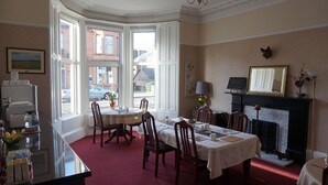 A dining room with a bay window, a fireplace, and a table set for four. - Lindean Guest House (Dumfries)