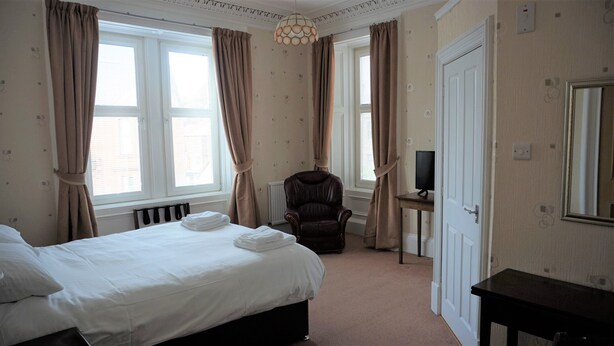 A hotel room with a bed, a chair, a desk with a computer, and a door. - Lindean Guest House (Dumfries)