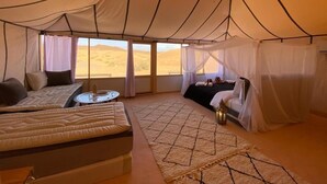 A tented room with a bed, a sofa, a small table, and a view of the desert. - Itran Royal Camp (Taouz)