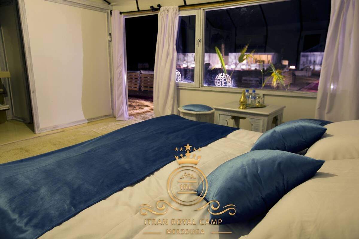 A bedroom with a bed, pillows, a nightstand, a window with curtains, and a view of the outside.