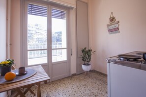 Une cuisine équipée d’une cuisinière, d’un évier, d’une fenêtre avec des stores, d’une plante en pot et d’une table avec un set de table et une orange.