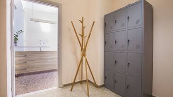 A room with a grey metal locker, a wooden tripod stand, and a wooden bench with drawers.