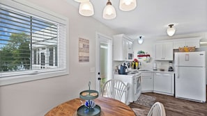 Een moderne keuken met witte kastjes, een eettafel met stoelen en een raam met zonwering.
