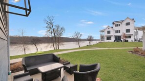 A patio with wicker furniture, a grassy lawn, and a view of a river and a white building. - Breathtaking River Front Views! (Ottawa)