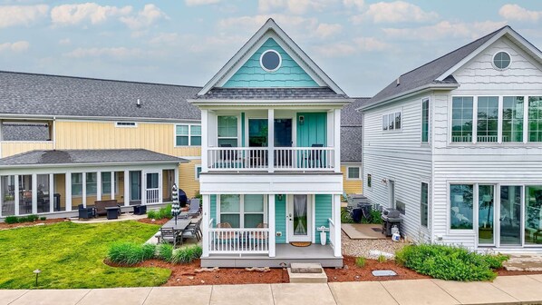 Une maison à deux étages avec un balcon, une terrasse couverte et un jardin devant.