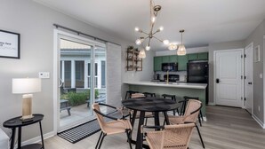 Una cocina moderna con armarios verdes, un refrigerador negro y un comedor con sillas de mimbre y una mesa redonda.