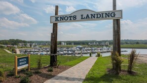 Satamassa on useita veneitä, puinen kyltti, jossa lukee ”KNOTS LANDING”, ja polku, joka johtaa nurmialueelle.