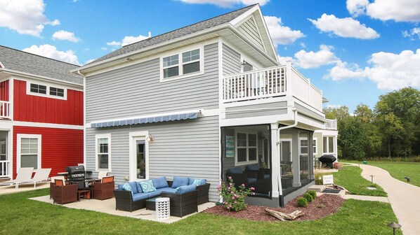 Una casa de dos pisos con balcón, un patio con mobiliario exterior y un jardín bien cuidado.