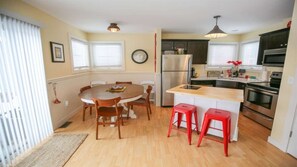 A compact kitchen with a dining area, a refrigerator, a microwave, and a wooden island with stools.