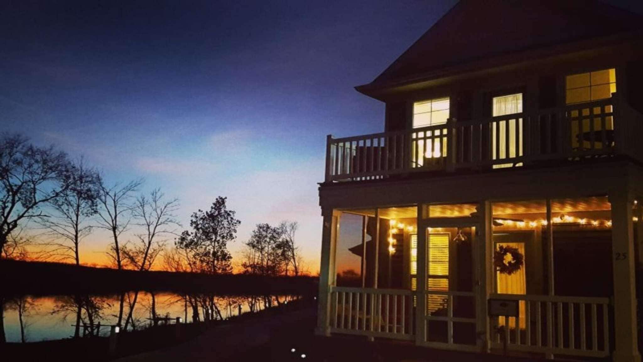 A two-story house with a balcony, large windows, and a view of a body of water.