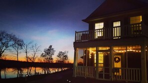 A two-story house with a balcony, large windows, and a view of a body of water.