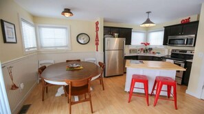 A kitchen with a wooden dining table, two red stools, a stainless steel refrigerator, and a clock on the wall.