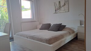 Une chambre à coucher comprenant un lit, des tables de chevet, une fenêtre et une œuvre d’art accrochée au mur.