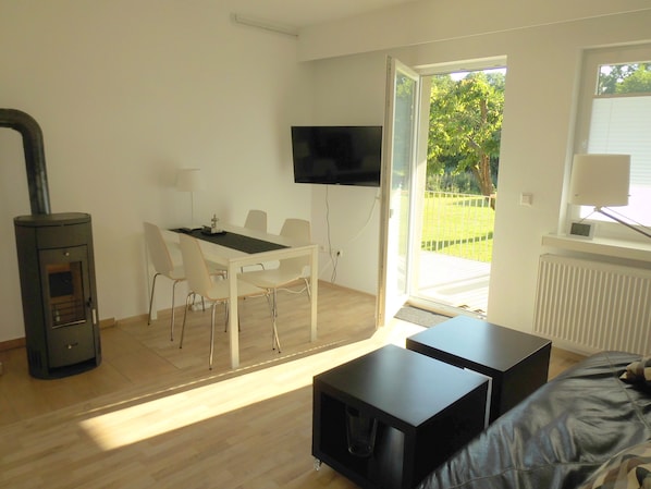 Ein modernes Wohnzimmer mit Essbereich, Kamin, Fernseher und Blick ins Freie.