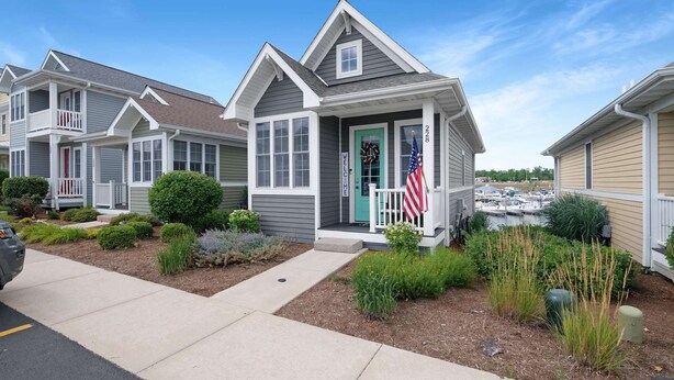 A row of single-story houses with a welcoming porch, a small garden, and a marina in the background.