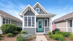 Une maison à deux étages avec une porte verte, une pancarte de bienvenue et un drapeau américain.