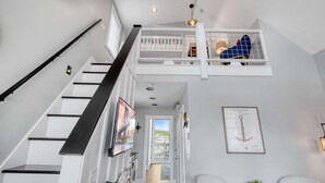 A multi-level interior with a staircase, a loft area with a railing, a framed patent document, and a view through a door.