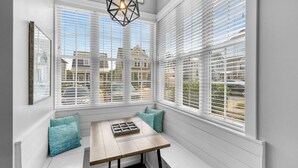 A bay window with white blinds, a wooden table with a tray, and teal cushions.