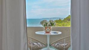 Un balcone con vista sul mare, un tavolo bianco con un vaso decorativo e sedie in vimini.