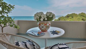 Un balcone con sedie in vimini, un tavolo con una rivista, un vaso decorativo con fiori e vista sul mare.