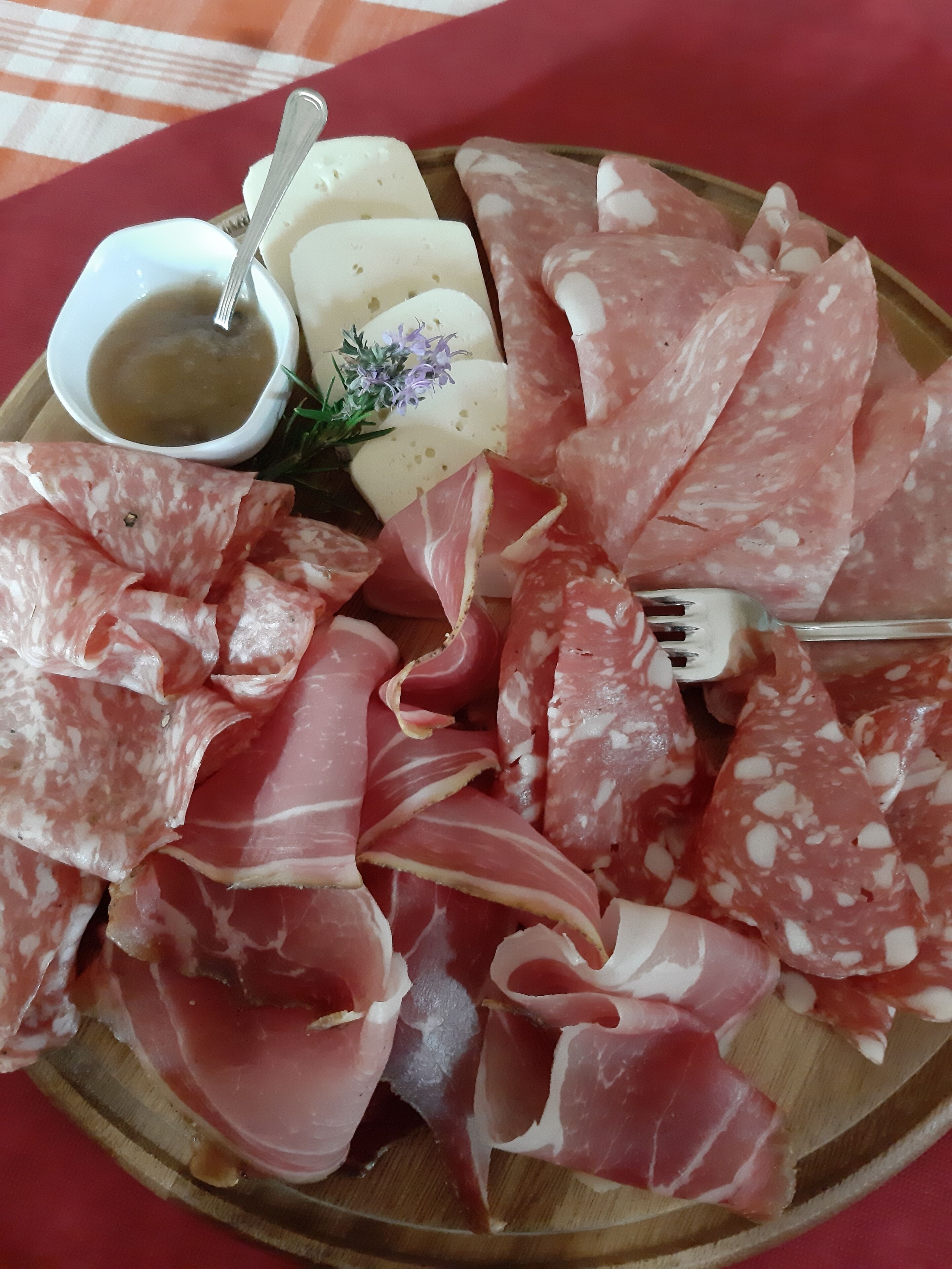 A wooden board with various types of cured meats, cheese, and a small bowl of sauce.