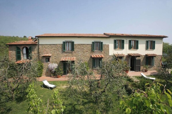 A two-story stone building with green shutters, a tiled roof, and a garden with lounge chairs. - Borgo La Casetta (Lamporecchio)