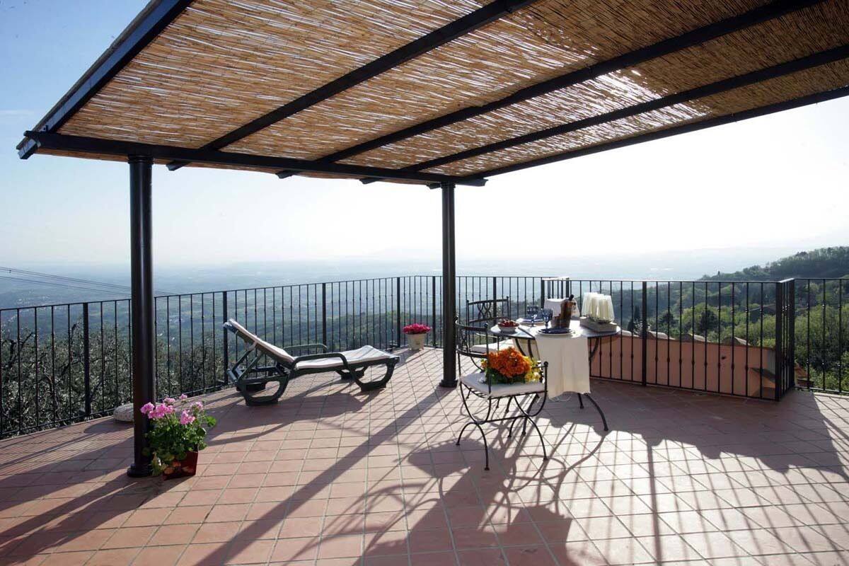 A covered terrace with a view of the landscape, a table with chairs, and a potted plant.