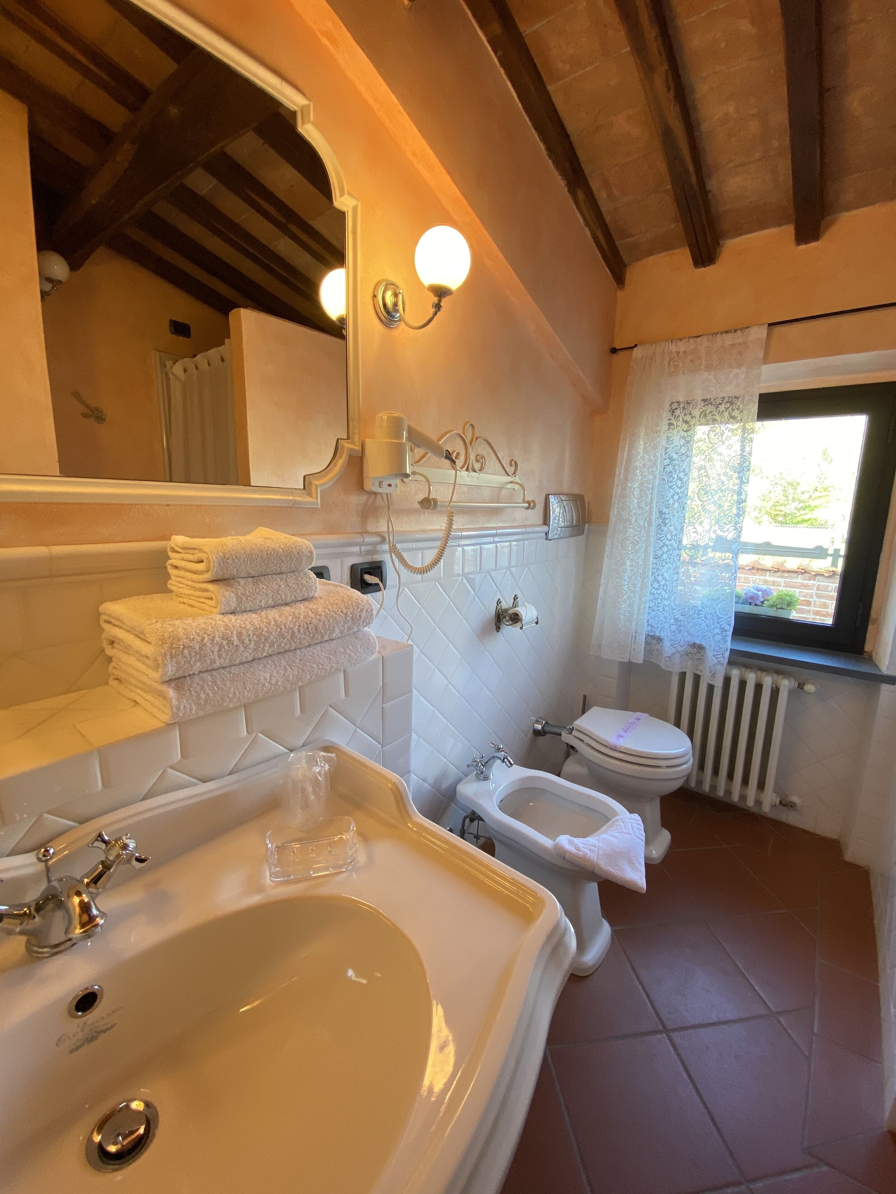 Un baño con bañera, lavabo e inodoro. Hay un perchero con toallas dobladas, un espejo y una ventana con vistas a la vegetación.