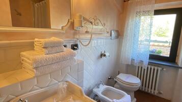 Un baño con bañera, lavabo e inodoro. Hay un perchero con toallas dobladas, un espejo y una ventana con vistas a la vegetación.