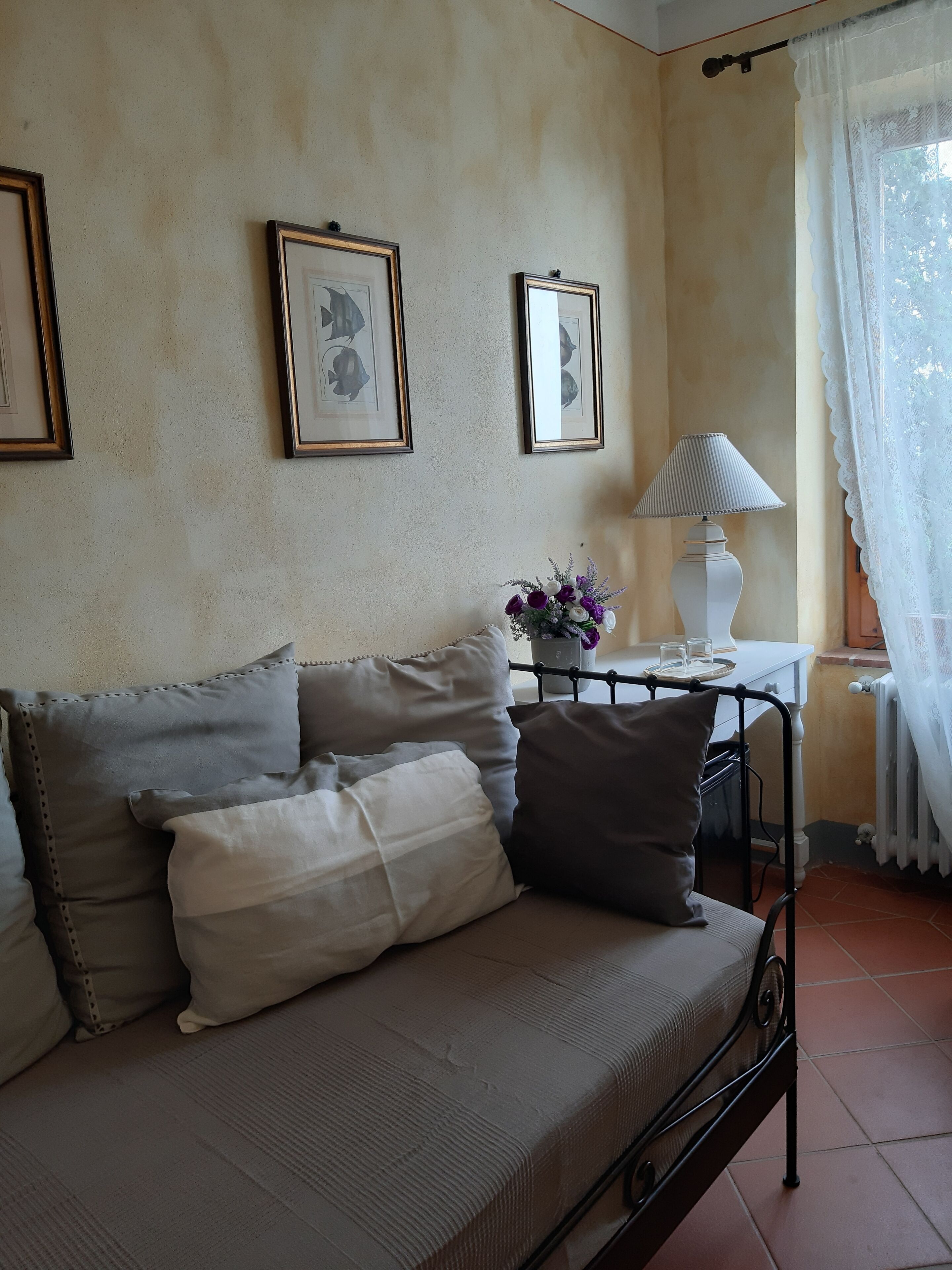 A cozy room with a sofa, framed pictures on the wall, a table with a lamp, and a window with curtains.