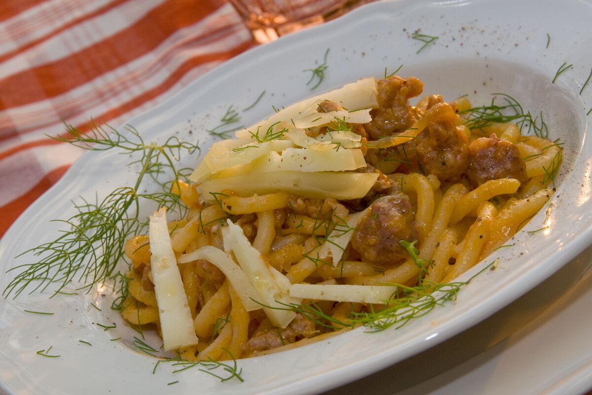 Un plat de pâtes aux boulettes, garni d’aneth et de fromage, servi dans une assiette blanche.