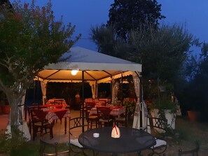 An outdoor dining area with tables and chairs under a tent, surrounded by trees. - Borgo La Casetta (Lamporecchio)