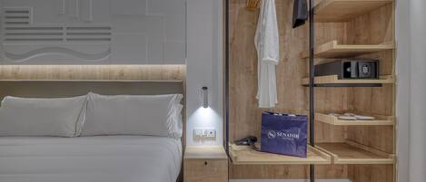 Una habitación de hotel moderna con cama, mesita de noche y estantería empotrada que incluye una bata y un bolso.