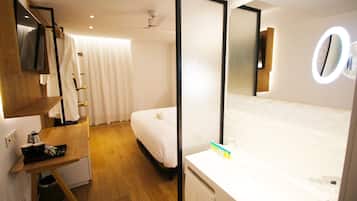 Quarto de hotel com uma cama, uma escrivaninha, um espelho e banheiro com pia e vaso sanitário.
