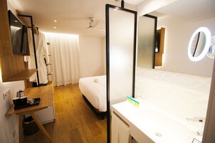 Quarto de hotel com uma cama, uma escrivaninha, um espelho e banheiro com pia e vaso sanitário.