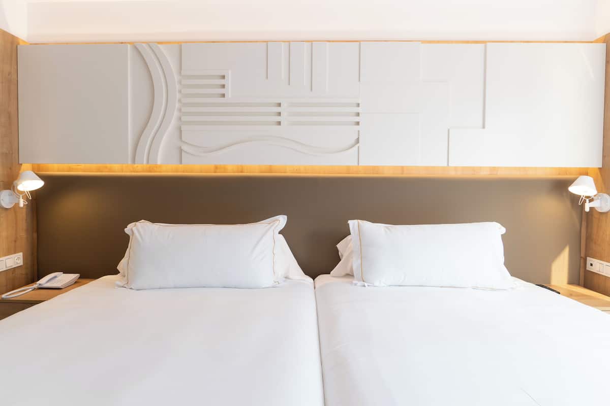 A hotel room with a double bed, a wooden headboard, and a wall-mounted light fixture.