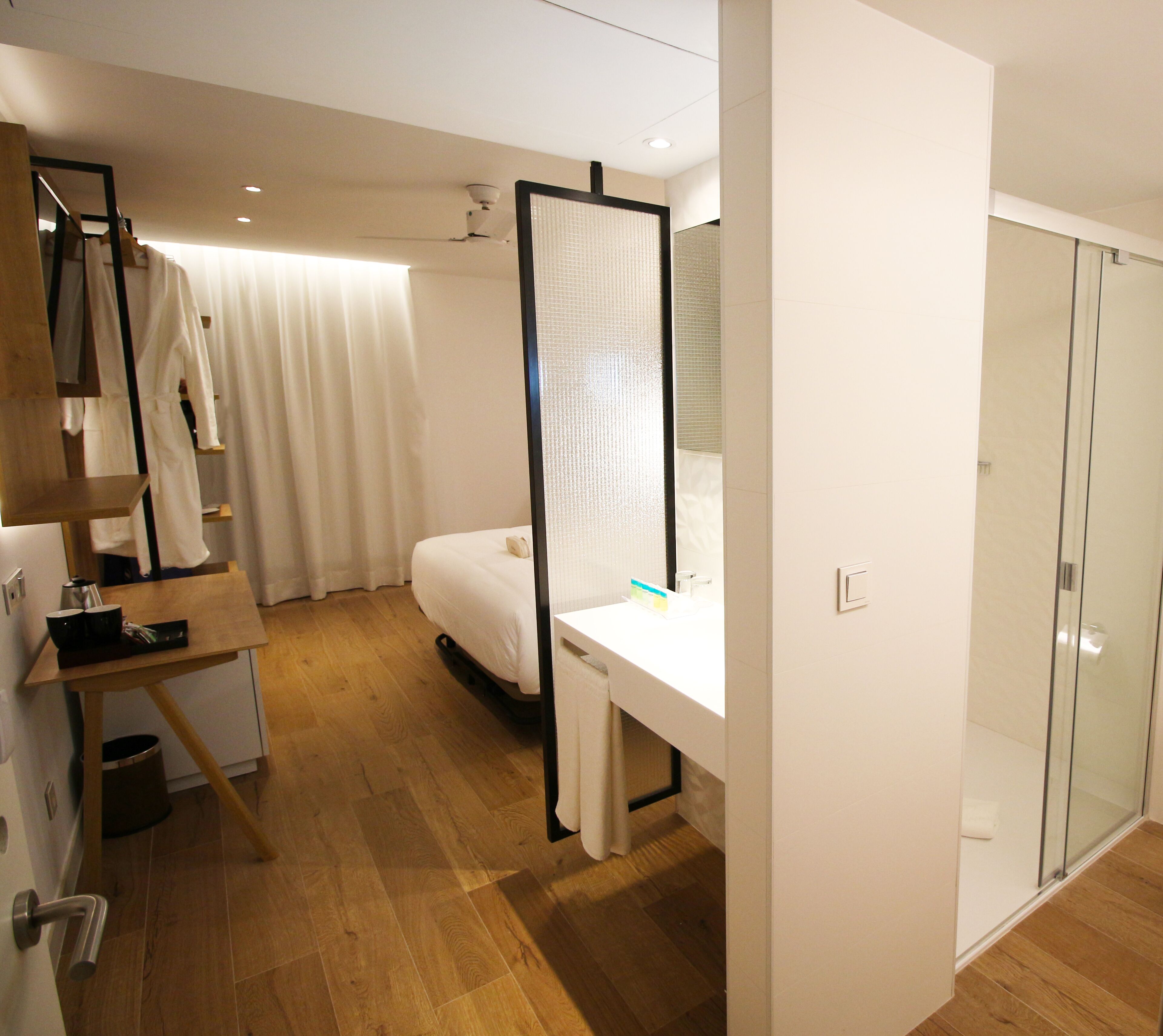 Une chambre d’hôtel moderne avec un plancher en bois, un lit, un bureau et une cabine de douche en verre.