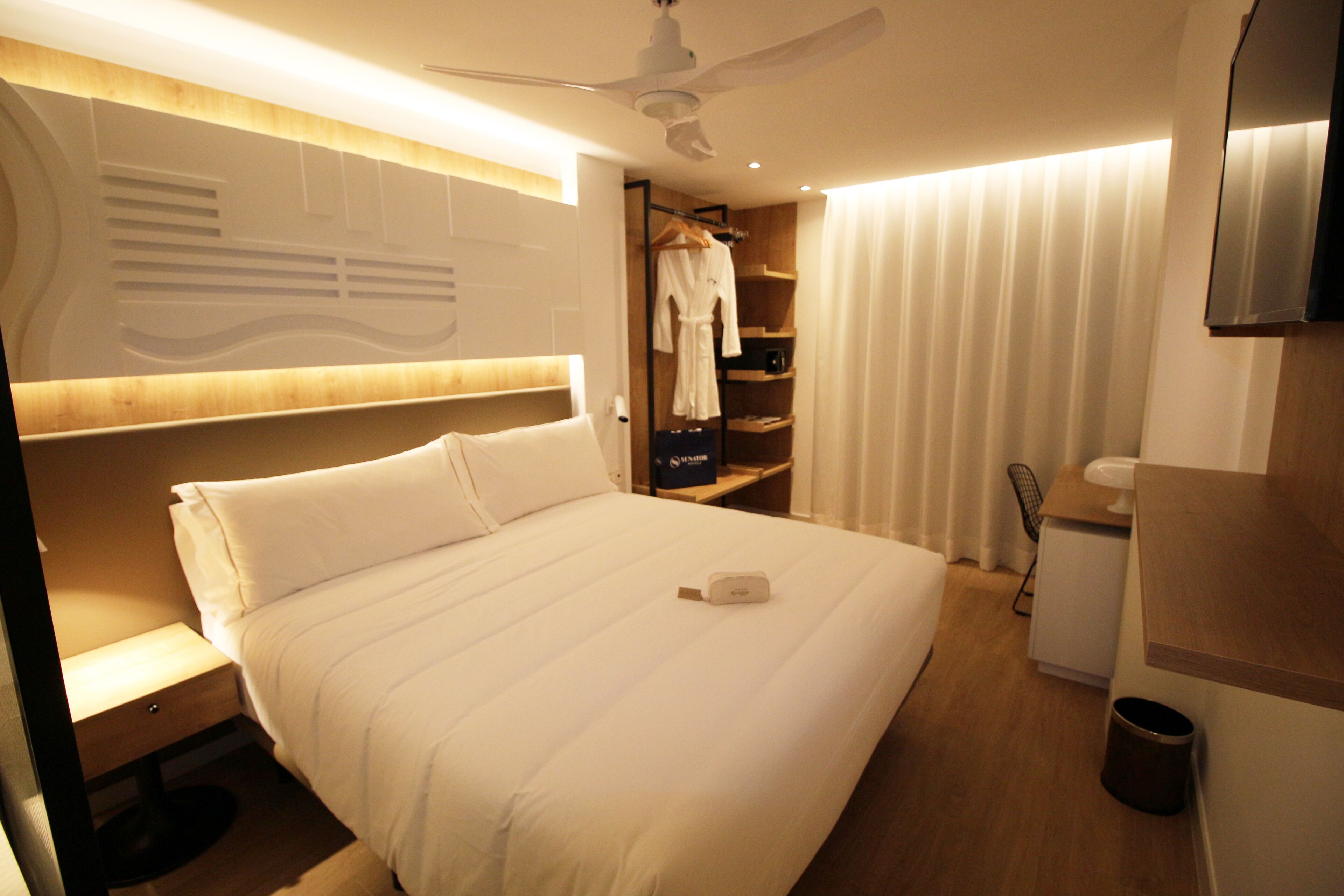 Una habitación de hotel con una cama grande, una mesita de noche, un armario y un ventilador de techo.
