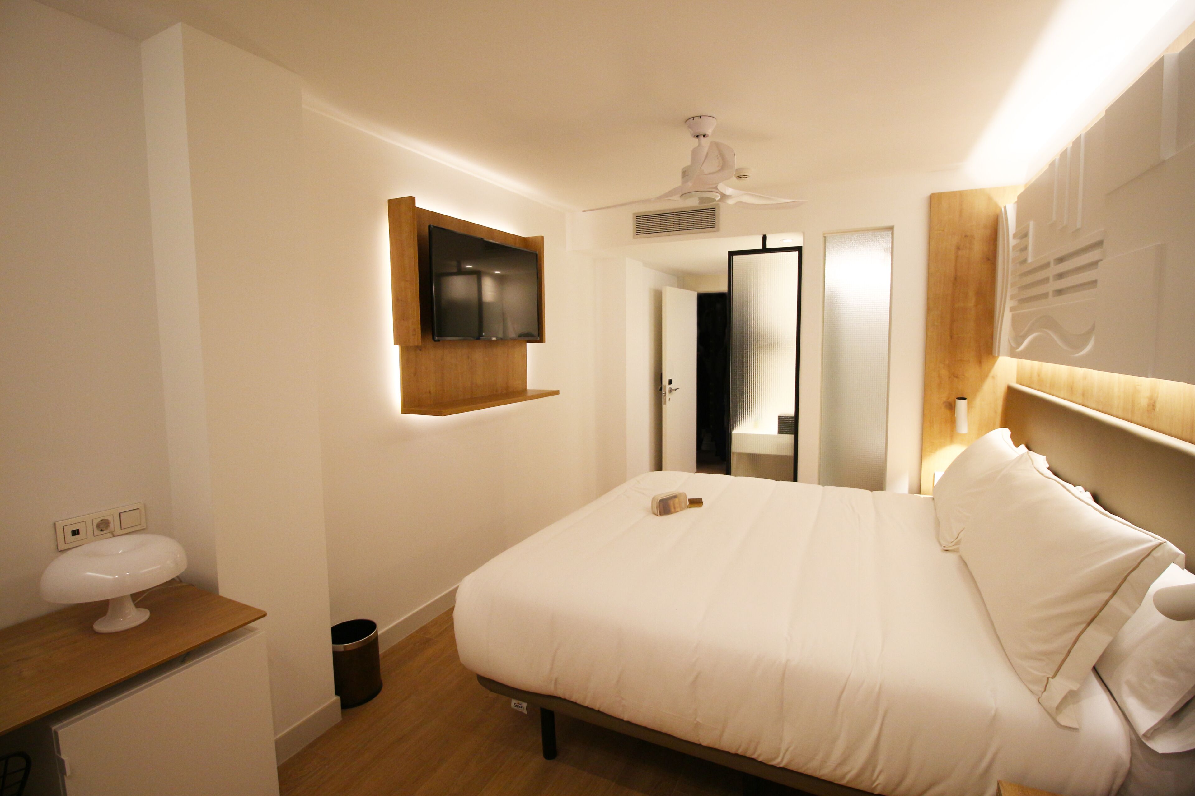 Ein Schlafzimmer mit Bett, Wandfernseher, Deckenventilator und Holz-Kopfteil.