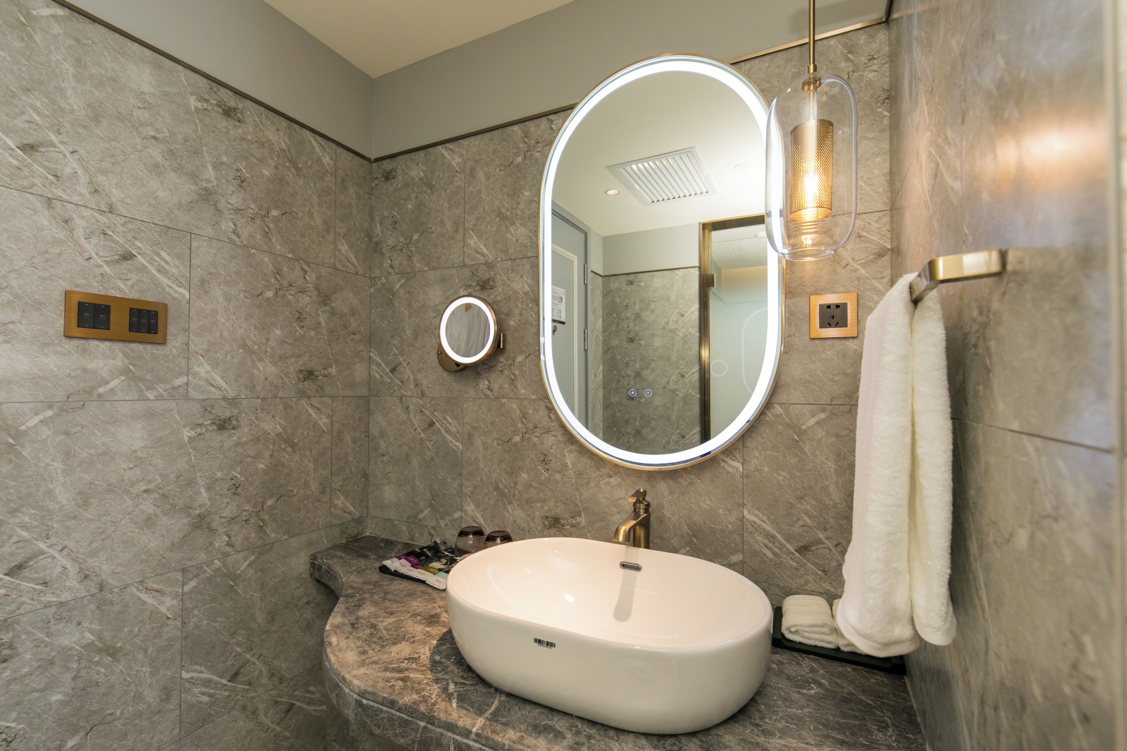 Une salle de bain avec un mur en marbre, un miroir rond, un lavabo et un porte-serviettes.