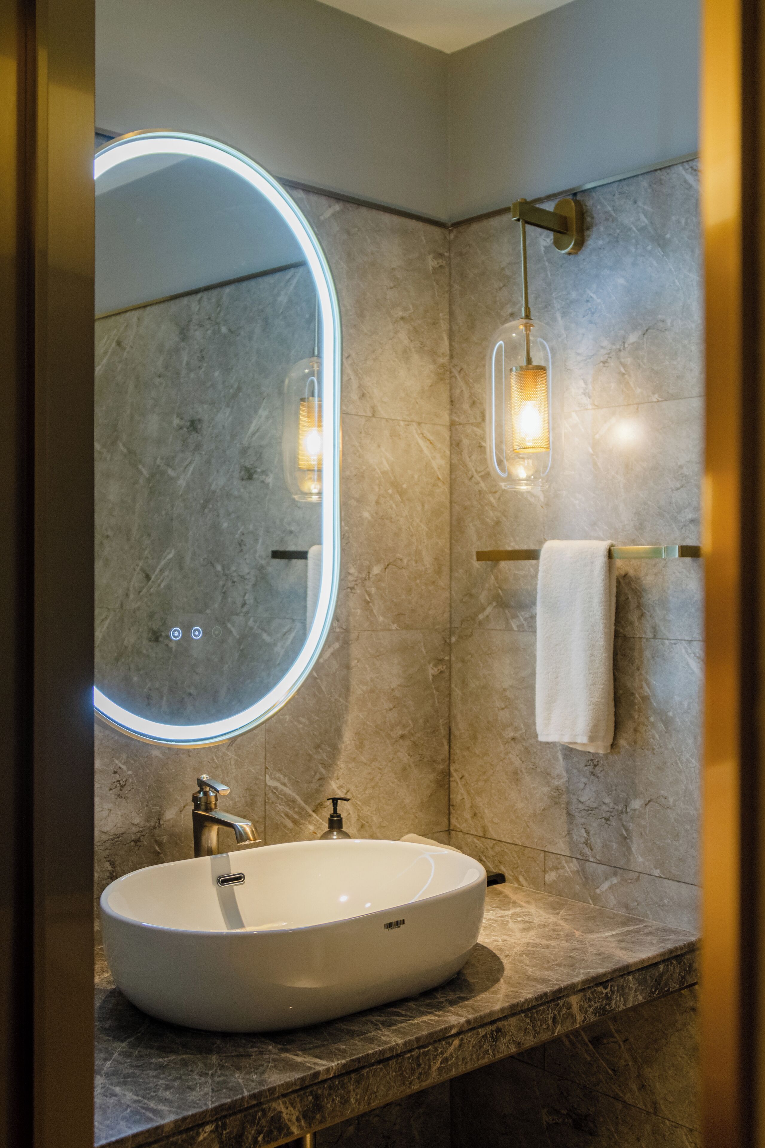 A bathroom with a large oval sink, a round mirror with a light, a towel rack, and a wall-mounted light fixture.