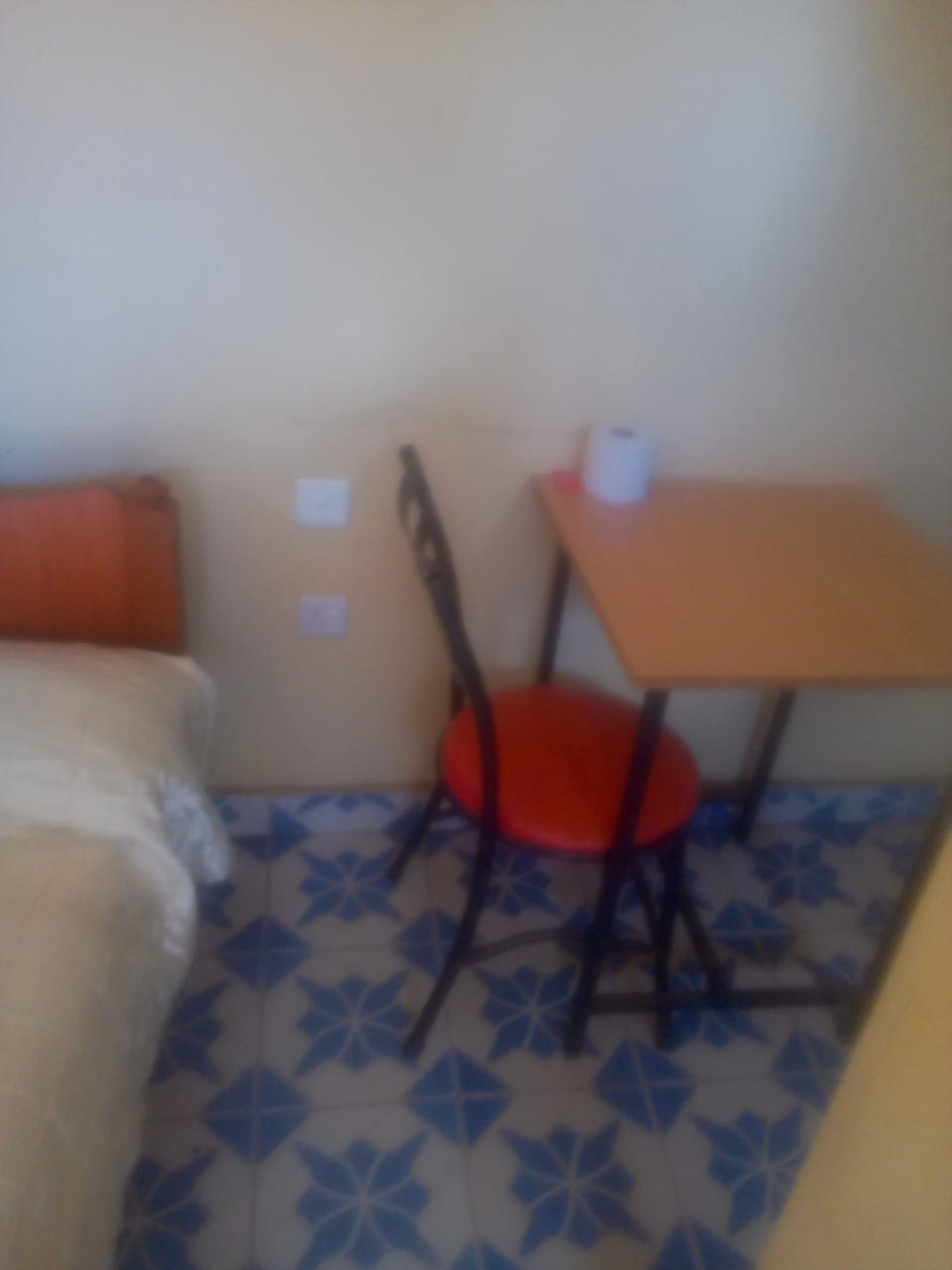 A small room with a bed, a table with a chair, and a tiled floor.