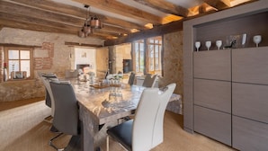 A rustic dining area with a large wooden table, modern chairs, and a stone wall. - Cottage Atypique (Mosnes)